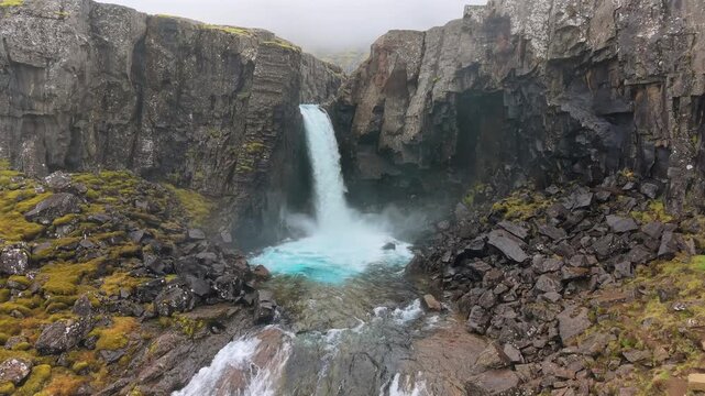 Dramatic aerial view of the beautiful Folaldafoss waterfall cascading into a stunning turquoise pool surrounded by rocky cliffs in Iceland