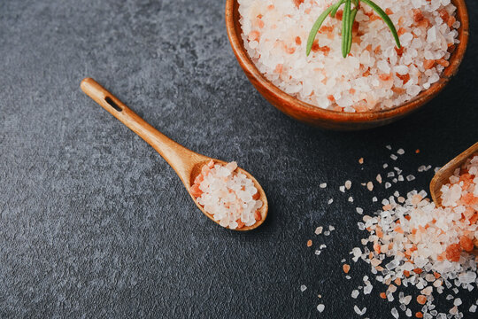 Pink Himalayan salt crystals in a wooden spoon and bowl on a dark background