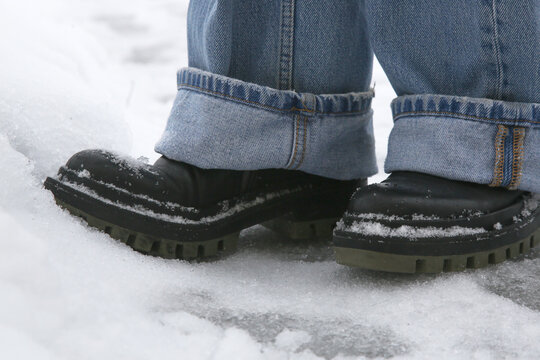 Danger of slipping. Person in chunky platform leather boots walking on snowy icey road
