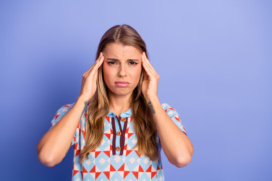 Young woman with stressed expression holding temples wearing a geometric patterned polo against a purple background model lifestyle shot