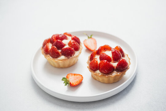 Two strawberry tartlets with fresh strawberries on a white plate