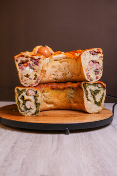 Cut sections of traditional Italian stuffed savory breads, showing rich fillings with cured meat, cheese, eggs, sausage and leafy greens, arranged on a wooden serving board.