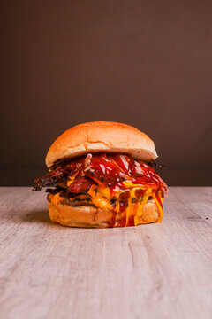 Close-up of a large gourmet bacon cheeseburger with beef patty, crispy bacon, melted cheese and sauces. Vertical food photography on a dark blurred background with generous copy space, 