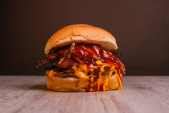 Close-up of a large gourmet bacon cheeseburger with beef patty, crispy bacon, melted cheese and sauces. Vertical food photography on a dark blurred background with generous copy space, 