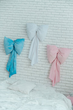 Three colorful plush bow pillows hang on a white brick wall above a soft white bed
