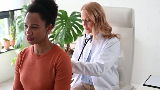 Female physician listening to patient's breathing with stethoscope during clinical examination. Black woman receiving professional respiratory health check