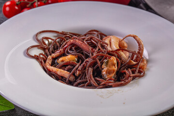 Dark squid ink spaghetti with octopus tentacles and mussels on white plate, cherry tomatoes and basil garnish, shallow depth of field © Andrei Starostin