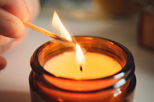 Hand lighting scented candle in brown glass jar, creating cozy atmosphere