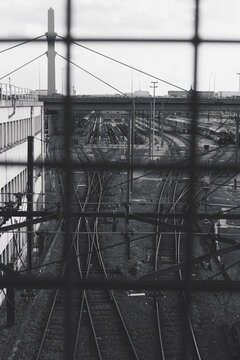 Monochrome railway tracks and industrial infrastructure seen through a metal grid create a layered geometric transport scene in an urban setting