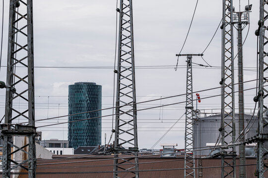 Electric railway infrastructure and overhead power lines create a dense industrial network with pylons and modern towers beneath a grey urban sky