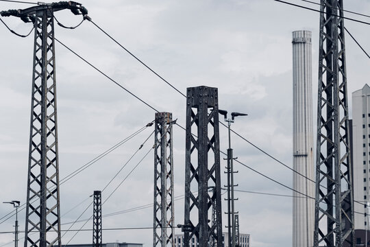Overhead power lines and railway infrastructure form a dense industrial pattern of pylons and utility structures beneath a pale urban sky
