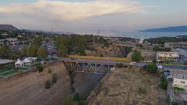 Slow pan drone shot above Corinth Canal at sunset, Greece. Bridges visible, cars crossing. Clear day, few clouds. Golden evening light