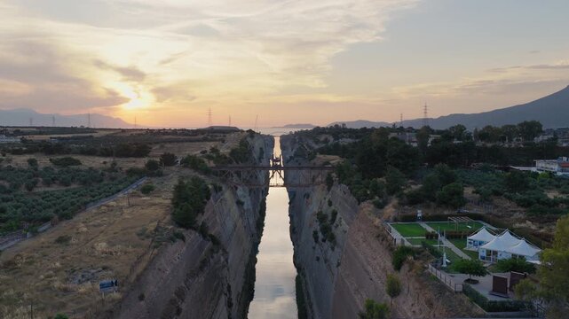 Aerial shot above Isthmus of Corinth, Greece at sunset. Bridges visible with crossing traffic. Clear day, few clouds. Golden light on waterway