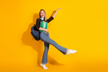 Young female student jumps with backpack and book against bright yellow background showing casual...