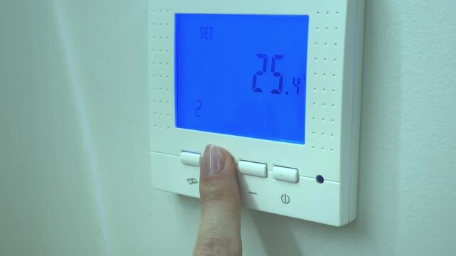 A hand adjusts temperature on a digital underfloor heating thermostat regulator, smart home comfort, energy saving, modern living style.