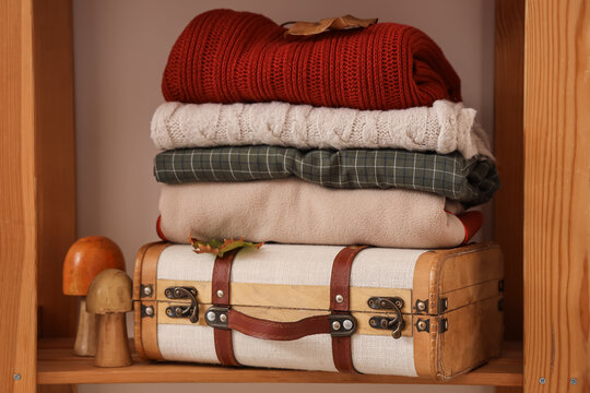 Autumn travel and seasonal preparation, stack of warm sweaters and cozy clothing on a vintage suitcase for fall vacation planning in a wooden shelf