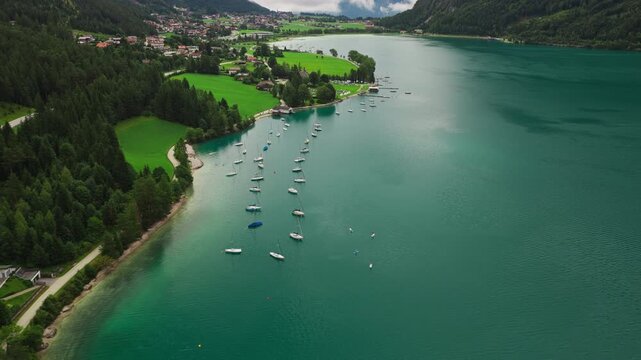 Boats on Lake Achensee in Tyrol, Austria, surrounded by blue alpine water, forested shoreline and mountain scenery - drone shot