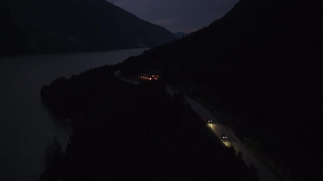 Cars Travel Along A Lakeside Road At Night Beside Lake Achensee In Tyrol, Austria. Aerial Shot