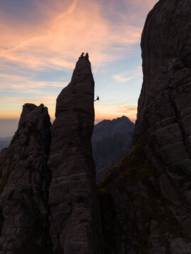 Aerial view of climbers on the sharp rock pinnacle of Punta Carina at sunset with dramatic mountain peaks in the background in Minucciano, Toscana, Italy.