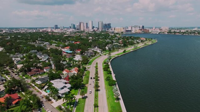 Aerial view of Bayshore Boulevard winding along Hillsborough Bay in Tampa's Hyde Park, with historic homes, the seawall promenade, and the downtown Tampa skyline in the distance.