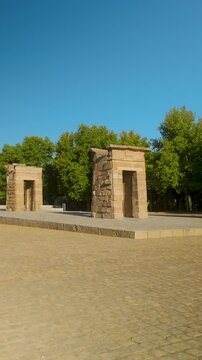 A vertical shot of the ancient Egyptian Temple of Debod in Madrid, Spain. This historic monument is surrounded by lush green trees under a bright sunny sky, perfect for travel and history content.