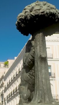 A closeup shot of the iconic El Oso y el Madrono statue in Puerta del Sol, Madrid, featuring historic architecture under a clear blue sky.