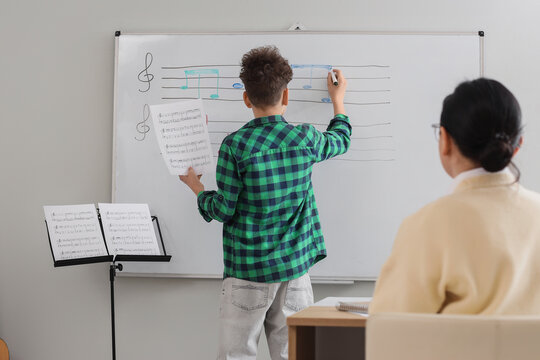Teenage boy writing music notes on whiteboard in classroom, back view