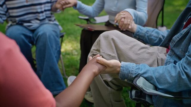 Diverse people sitting in circle holding hands during outdoor psychotherapy session. Visual concept ideal for mental health campaigns and community therapy projects