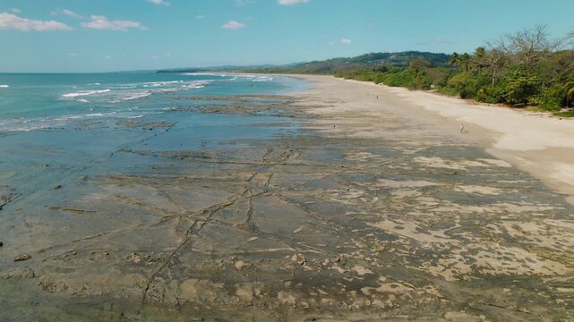 Aerial view of wide sandy beach with tidal rock patterns and distant hills