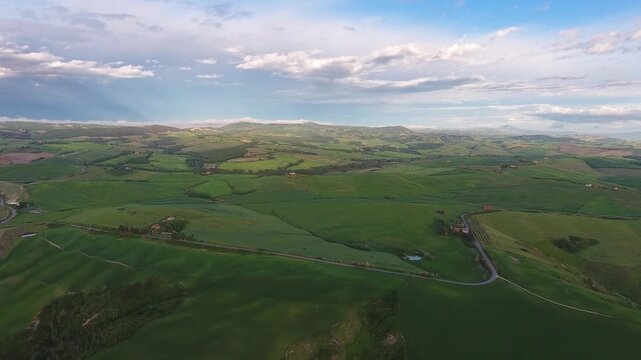 Aerial view of rolling green hills and winding roads across the landscape of Tuscany, Italy.