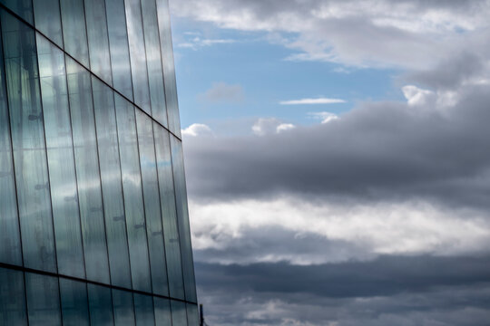 Reflective glass facade in Oslo Norway stands beside dramatic clouds creating a minimal urban composition of architecture sky and light