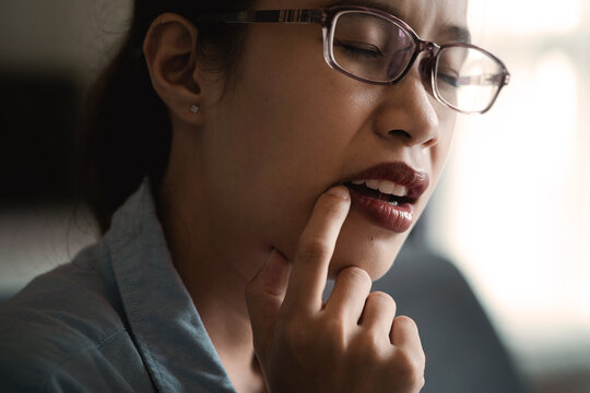 Woman Wearing Glasses Pressing Her Hand Against Her Cheek in Pain from a Toothache Beside a Bright Window