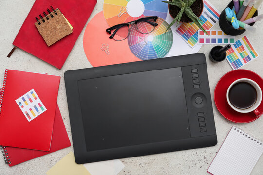 Graphic tablet with stationery and coffee cup on light background, top view