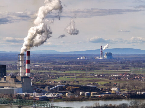 Aerial view of Nikola Tesla A thermal power plant with tall chimneys emitting smoke, industrial facilities, and surrounding fields near the Sava river in Urovci, Grad Beograd, Serbia.