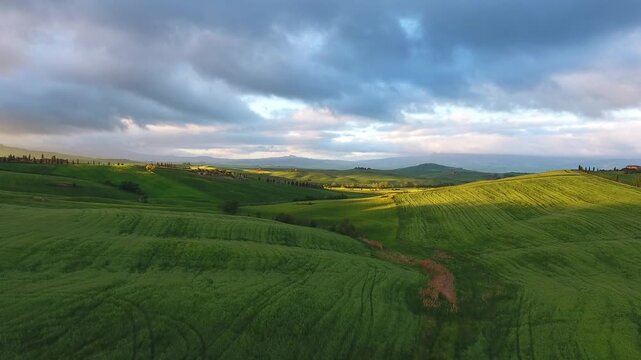 Aerial view of rolling green hills and lush meadows under a dramatic cloudy sky in the countryside of Tuscany, Italy.