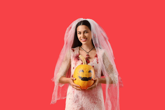 Young woman dressed for Halloween as dead bride with pumpkin on red background