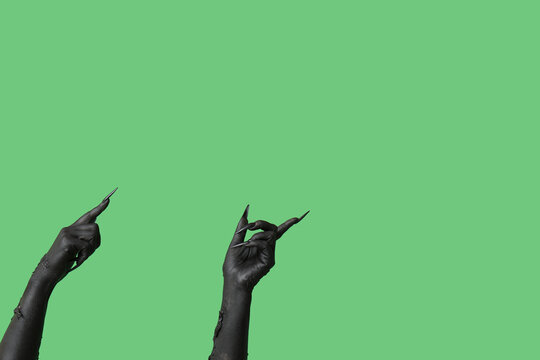 Black hands of witch pointing at something on green background. Halloween celebration