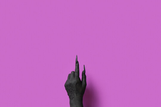 Black hand of witch pointing at something on purple background. Halloween celebration
