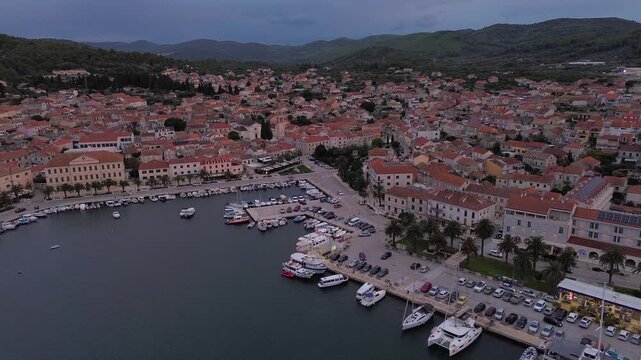 Aerial view of the harbor and town of Vela Luka, featuring boats moored at the waterfront, historic buildings, and surrounding hills in Vela Luka, Croatia.