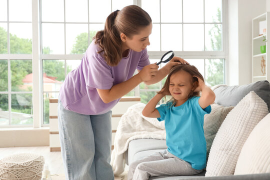 Mother with magnifier checking her little daughters head with pediculosis at home