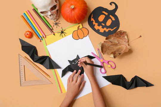 Child with supplies making Halloween decorations and origami bats on orange background