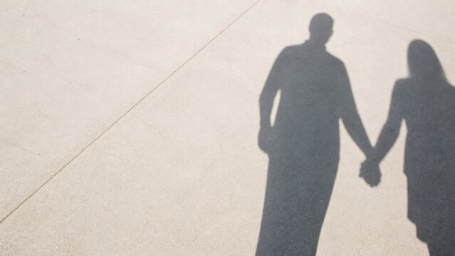 Couple holding hands shadow silhouette cast upon concrete pavement captures romantic connection and unity through minimalist natural lighting and overhead perspective