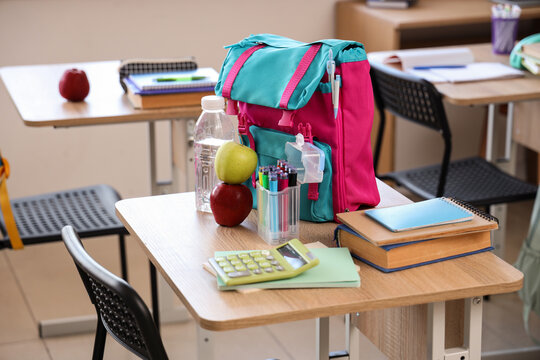 Apples with water bottle and backpack on desk in classroom