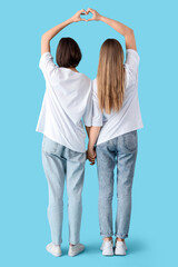 Obraz premium Female friends making heart gesture on blue background, back view