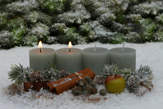 A natural Advent arrangement on a wooden disc in the snow. Two candles are lit for the second Sunday of Advent.