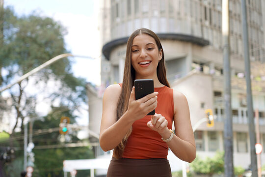 Smiling Brazilian woman using smartphone on sunny day in financial district of Sao Paulo, Brazil