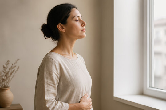 Femme pratiquant une respiration consciente pr&egrave;s d'une fen&ecirc;tre