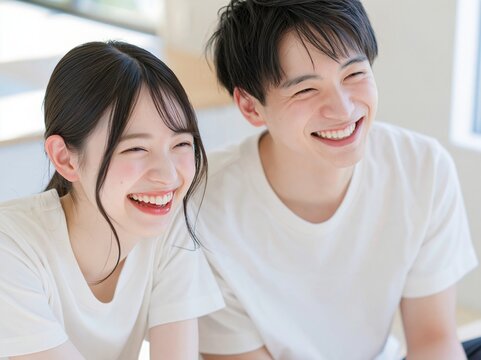 部屋の中で並んで笑顔を弾けさせ楽しそうに大笑いする若い男女