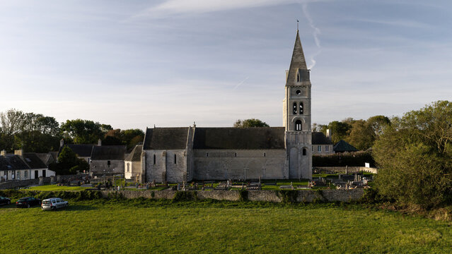 Aerial view of the historic Eglise Notre-Dame de Colleville-sur-Mer with its stone bell tower and surrounding cemetery in Colleville-sur-Mer, Normandie, France.