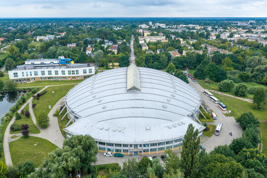 Aerial view of the Pruszkow Velodrome, a large indoor cycling arena with a domed roof, surrounded by parkland, trees, and urban infrastructure in Pruszkow, Masovian Voivodeship, Poland.